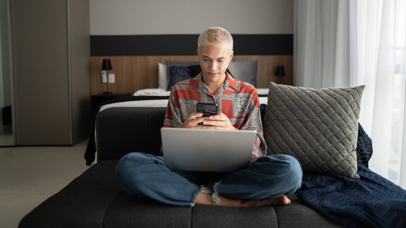 woman using phone and laptop on sofa